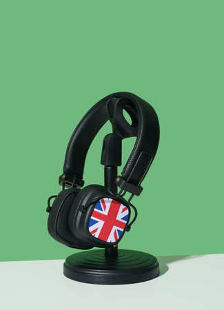 closeup of a pair of black headphones patterned with the flag of the united kingdom, in a black desktop stand, on a white surface, against a green backgroundの写真素材