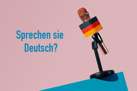 a microphone patterned with the german flag, in a black stand on a blue table, and the question do you speak german written in german on a pink backgroundの写真素材