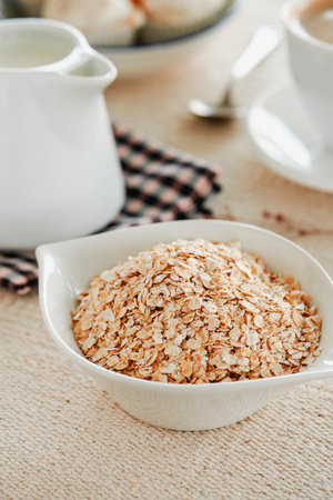 closeup of a white ceramic bowl with some rolled oats next to a white ceramic creamer with some plant milk on a table set with a beige tableclothの写真素材