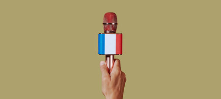closeup of the hand of a man holding a microphone patterned with the french flag , on a brown background, in a panoramic format to use as web banner or headerの写真素材