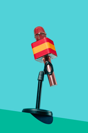 closeup of a microphone patterned with the spanish flag, in a black stand placed on a green surface, in front of a blue backgroundの写真素材