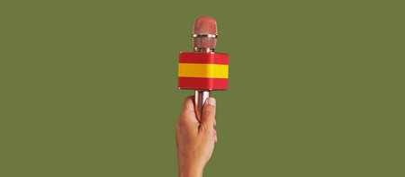 man holding a microphone patterned with the flag of spain on a green background, in a panoramic format to use as web banner or headerの写真素材