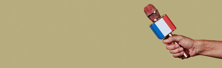 a man holds a microphone patterned with the french flag , on a brown background with some blank space on the left, in a panoramic format to use as web bannerの写真素材