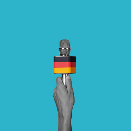 the hand of a man in black and white holds a microphone patterned with the german flag on a blue backgroundの写真素材