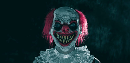 a mad evil redhead clown, wearing a white and red striped costume with a white ruff, stands with...
