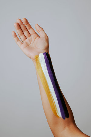 closeup of the arm of a person with the non-binary pride flag painted in it, against a pale gray backgroundの写真素材