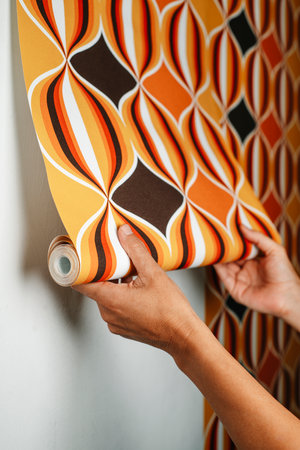 a caucasian man attaches a geometric patterned wallpaper to a white wallの写真素材