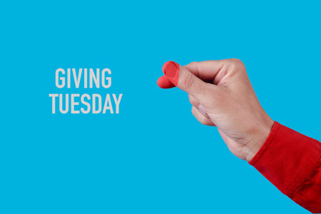 the text giving tuesday and a man doing the finger heart gesture, with the tips of his fingers painted red in the shape of a heart, on a blue backgroundの写真素材
