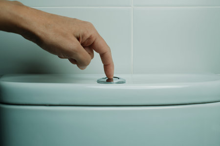 a man is about to flush the toilet, by pressing the button, in a tiled bathroom after using itの写真素材
