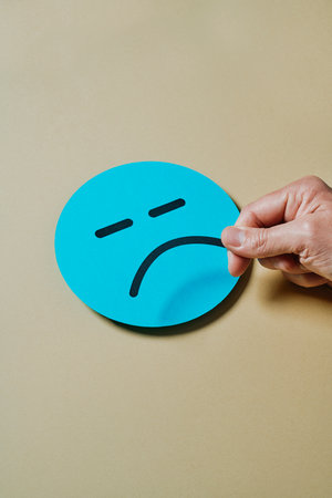 a man places a sad mouth on a blue cardboard face on a yellow backgroundの写真素材