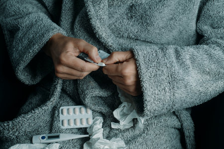 closeup of an ill man at home, wearing a warming gray house robe, surrounded by used tissues, about to take a pillの写真素材