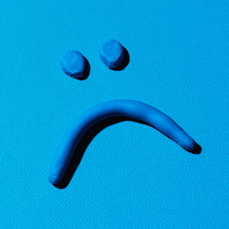 closeup of a sad face made with blue modelling clay on a blue leather backgroundの写真素材
