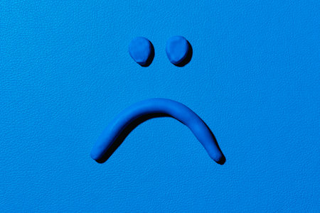 a sad face made with blue modelling clay on a blue backgroundの写真素材