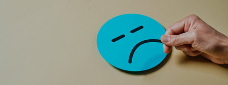 man setting a sad mouth in a blue cardboard face on a yellow background, in a panoramic format to use as web bannerの写真素材