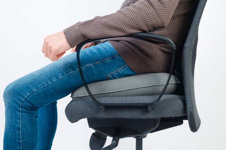a caucasian man wearing casual clothes uses an inflatable ring cushion to seat on an office chairの写真素材