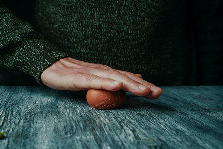closeup of a man rolling a hard-boiled egg against the table to remove its shellの写真素材