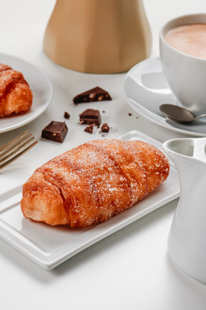 closeup of a xuixo de crema, a pastry filled with custard typical of catalonia, spain, on a white ceramic plate, next to a cup of coffee on a set tableの写真素材