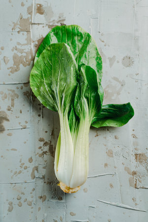 high angle view of a fresh bok choy placed on a gray textured surface splashed with waterの写真素材