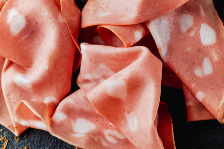 closeup of some slices of mortadella on a black textured surface