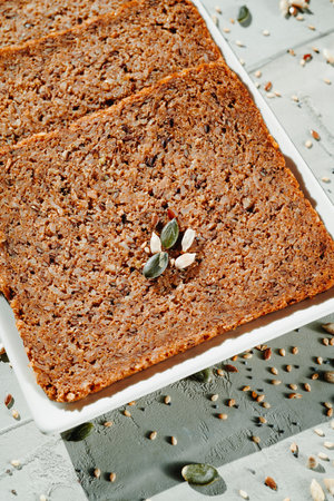 some slices of rye bread with flax seeds in a white rectangular ceramic plate placed on a gray textured surfaceの写真素材