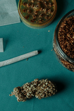 closeup of a cannabis bud on a table next to a used herb grinder, a jar with some rolling tobacco and a spliffの写真素材