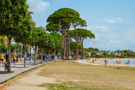 Cambrils, Spain - June 9, 2024: People walking by Passeig de Ponent promenade in Cambrils, next to the Ardiaca Beach, enjoying the good weather of a sunny spring Sundayのeditorial素材