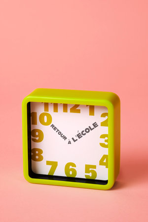 a green square clock, with green numbers and the text back to school written in french instead of the hour and the minute hands, on a pink backgroundの写真素材