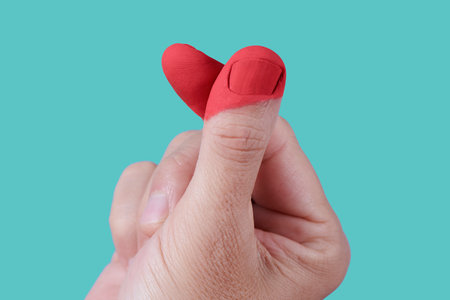 closeup of the fingers of a man doing the finger heart gesture, with his fingers painted red to form a heart as well, on a green backgroundの写真素材