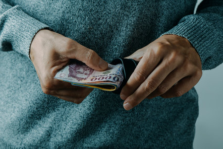 closeup of a man, wearing a gray pullover, taking out or putting some hungarian forint bills into his walletの写真素材
