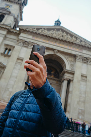 closeup of a man taking a selfie in front of St Stephens Basilica in Budapest, Hungary, with his smartphone, on an autumn dayの写真素材