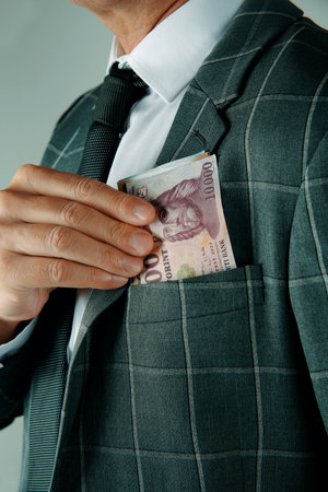 a businessman, wearing an elegant gray suit, takes out or puts some hungarian forint notes into the pocket of his jacket, indoorsの写真素材