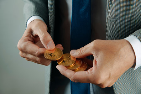 a businessman, wearing an elegant gray suit, white shirt and blue tie, has some bitcoins in his hands indoorsの写真素材
