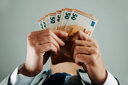 a businessman, wearing a suit, white shirt and tie, seen from below, counts some euro banknotes indoorsの写真素材