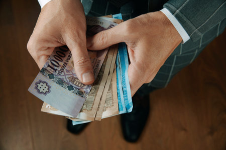 a businessman, wearing an elegant gray suit, counts some hungarian forint notes whiles is standing...