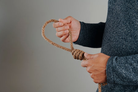 a man holds a jute rope with a noose, on a gray background with some blank space on the leftの写真素材