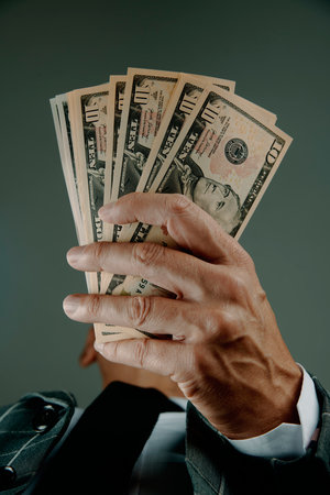 closeup of a businessman, wearing an elegant gray suit, with a wad of dollar banknotes in his hands, against a gray backgroundの写真素材