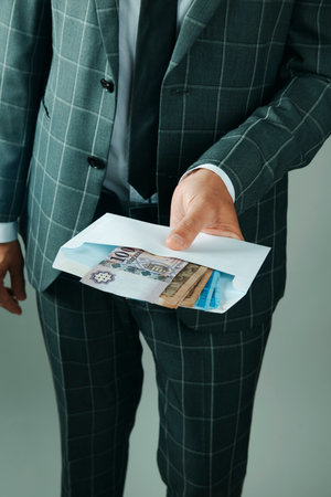 a businessman, in an elegant gray suit, has an envelope with some hungarian forint notes in his hand which he offers to the observerの写真素材