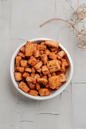 high angle view of a white bowl with some marinated tofu cubes, served as snack, on a rustic concrete surfaceの写真素材