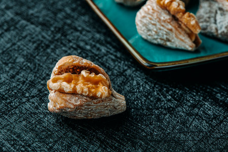 closeup of a a dried fig filled with half wwalnut on a table next to a plate with more dried figs filled with walnutsの写真素材