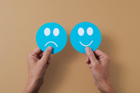 closeup of the hands of a man holding a blue paper sad face, in his left hand, and a blue paper...