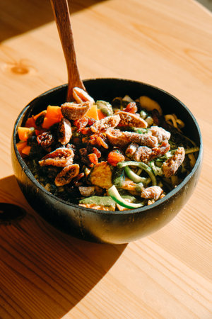 closeup of a salad, with vegetables, legumes and fruits such as dry figs and apricots, served on a coconut bowl placed on a round  tableの写真素材