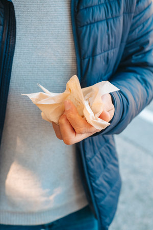 a man, wearing jeans, a gray sweater and a blue jacket, is about to use a recycled paper tissue while is standing outdoorsの写真素材