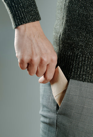 a man, wearing gray trousers and a green knitted sweater, is about to take a paper tissue out of the pocket of his trousersの写真素材