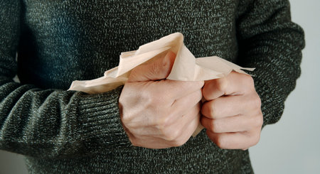 closeup of a man, wearing a green knitted sweater, about to blow his nose with a recycled paper facial tissue, indoorsの写真素材