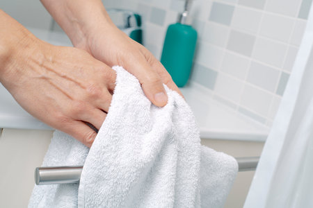 closeup of a man drying his hands with a white terry towel in a tiled domestic bathroomの写真素材