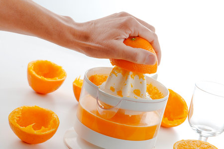 closeup of a man squeezing some oranges on an electric juicer to prepare a fresh orange juiceの写真素材