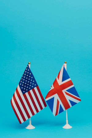a flag of the United States and a flag of the United Kingdom standing side by side on a blue background with some blank space on topの写真素材