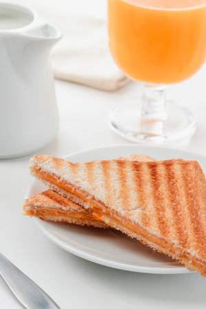 closeup of a freshly grilled ham and cheese sandwich, next to a glass of orange juice and a creamer with milkの写真素材