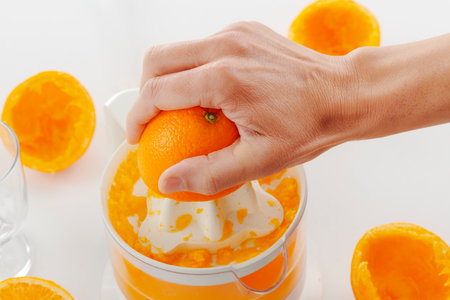 closeup of a man making an orange juice with an electric juicer, on a white surfaceの写真素材