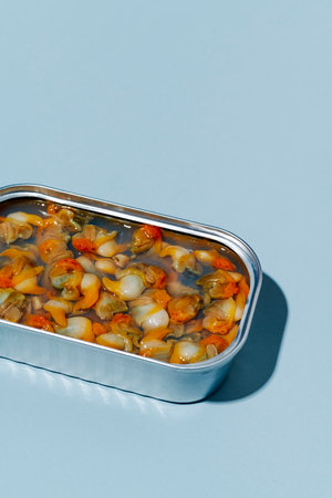 closeup of an open can of tinned cockles on a light blue background with some blank space on topの写真素材